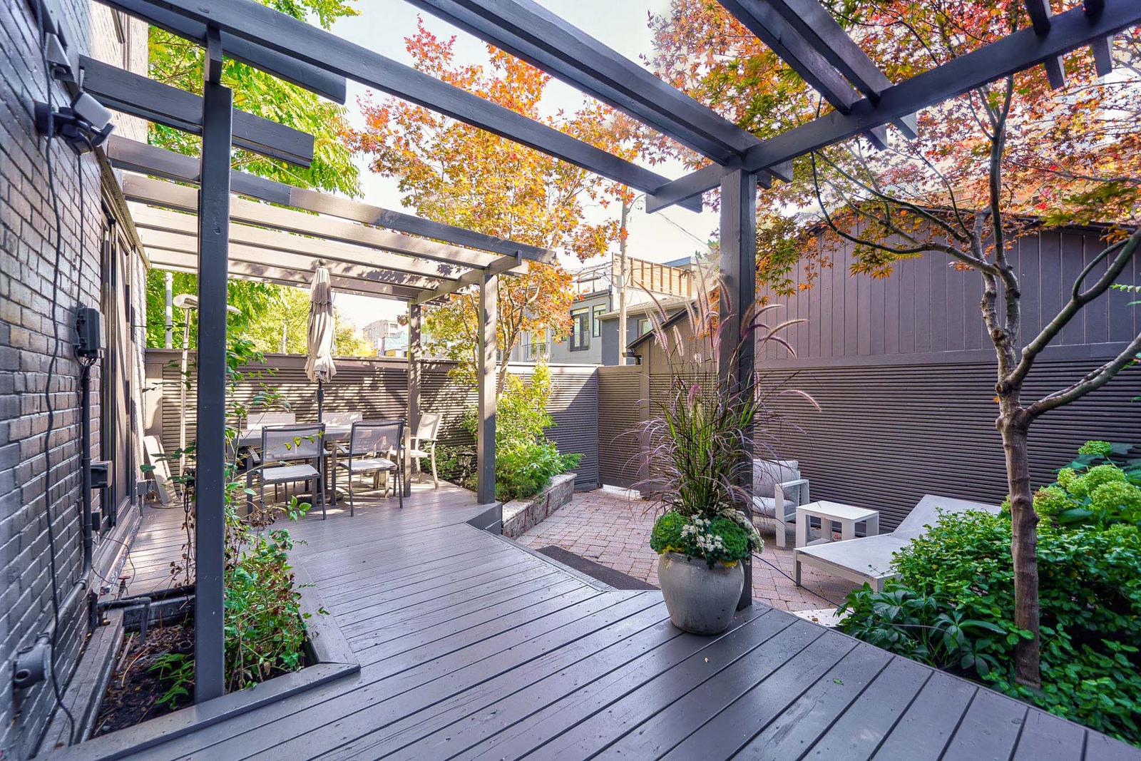 In the backyard: a pergola covered deck, an interlocking stone patio and greenery. 