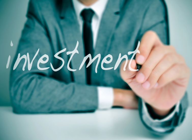 A person in a suit is writing the word "investment" with a marker, focusing on the letters.