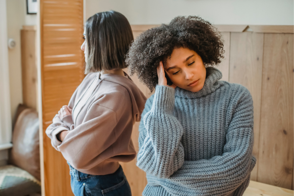 Two female housemates are standing back-to-back and look upset with each other. A good tip for housemates is to tackle issues as they arise. 