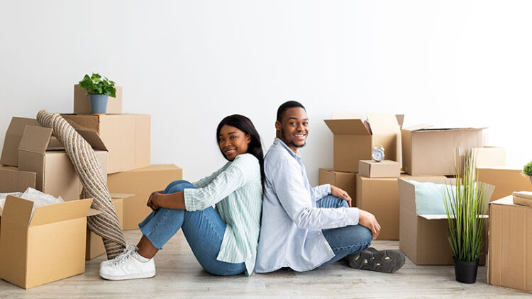 A couple sits on the floor surrounded by moving boxes in their new home. U-Haul moving supplies, such as packing paper, are great for keeping items secure and safe inside moving boxes