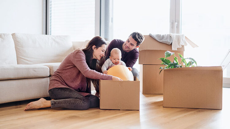 A couple sits on the floor with their baby as they open an item out of their moving box in the living room of the family’s new home. U-Haul stretch wrap is one of the many moving supplies you can get from U-Haul that’ll help create a successful move for you