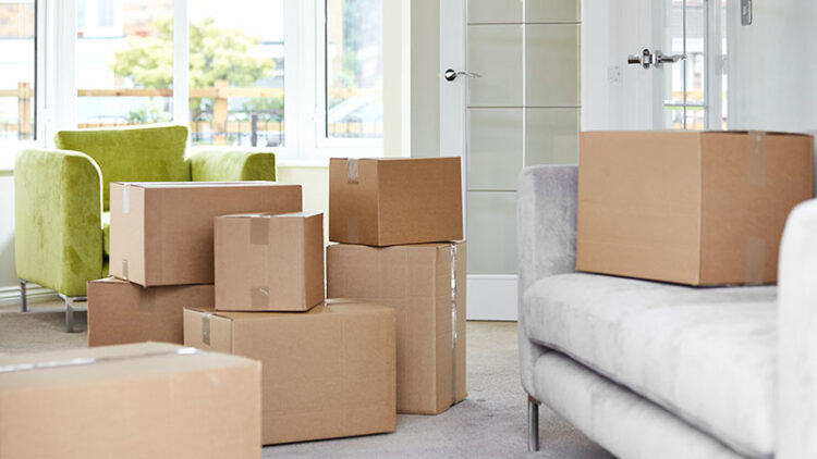 A couch, chair, and moving boxes sit in a living room waiting to be loaded into a rental truck. Labels for moving boxes and box markers and a knife are great moving supplies to use to help keep you organized and efficient on moving day