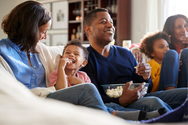 A family is sitting on a sofa watching a movie and eating popcorn to celebrate Father's Day. 