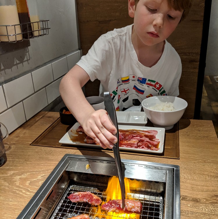 Boy grilling meat on a table inside a Japanese restaurant, Yakiniku Japanese cuisine