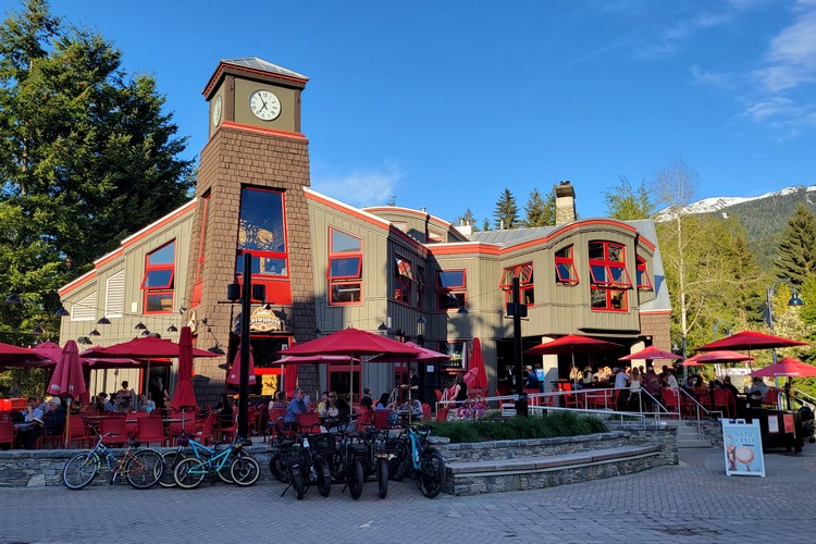 exterior of Whistler Brewpub with clock and mountains in the backdrop, Whistler Village Stroll in the summer