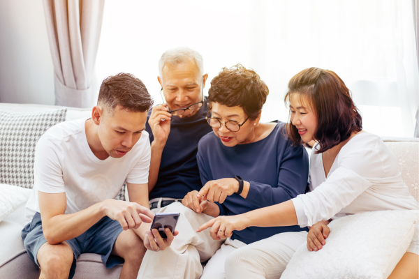 A multi-generational family is sitting on a sofa and looking at a mobile phone. A family plan can help you find the best mobile phone deal in Canada.