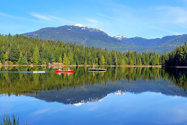 a red canoe cuts across the calm reflection on the water at Lost Lake in Whistler, British Columbia